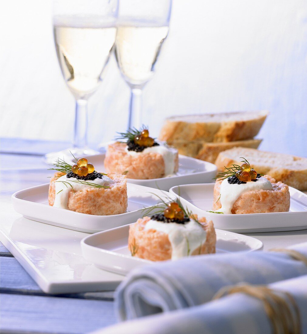 Four portions of salmon tartare on plates, glasses of sparkling wine