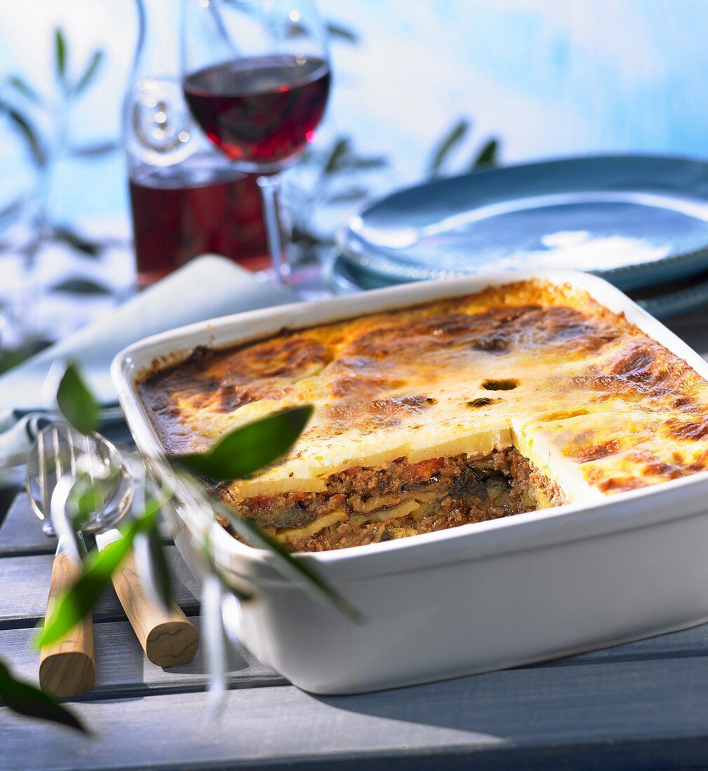 Moussaka in a baking dish and a glass of red wine