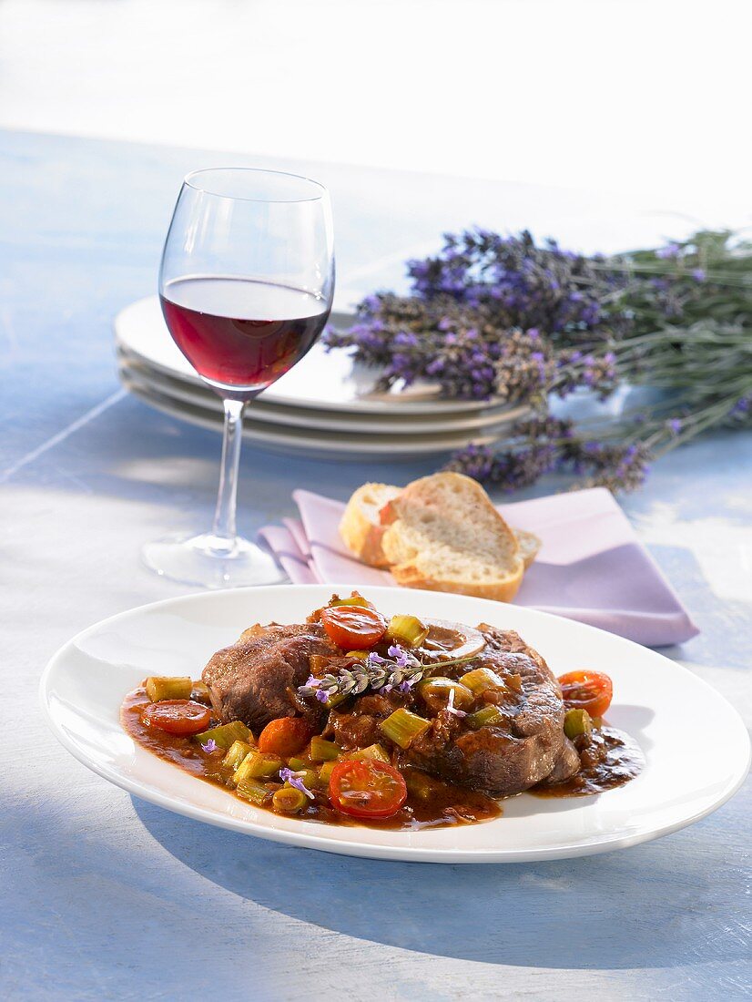 Eine Scheibe Ossobuco mit Schmorgemüse und einem Glas Wein