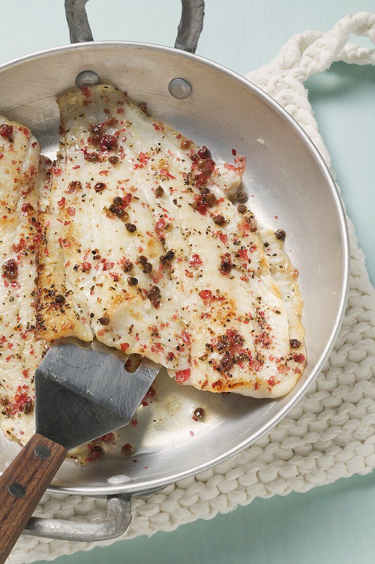 A fried peppered plaice with spatula in a frying pan