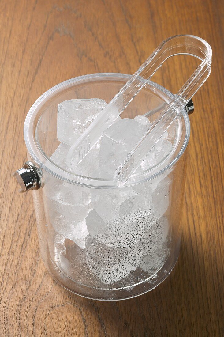 Ice cubes in transparent champagne bucket with tongs
