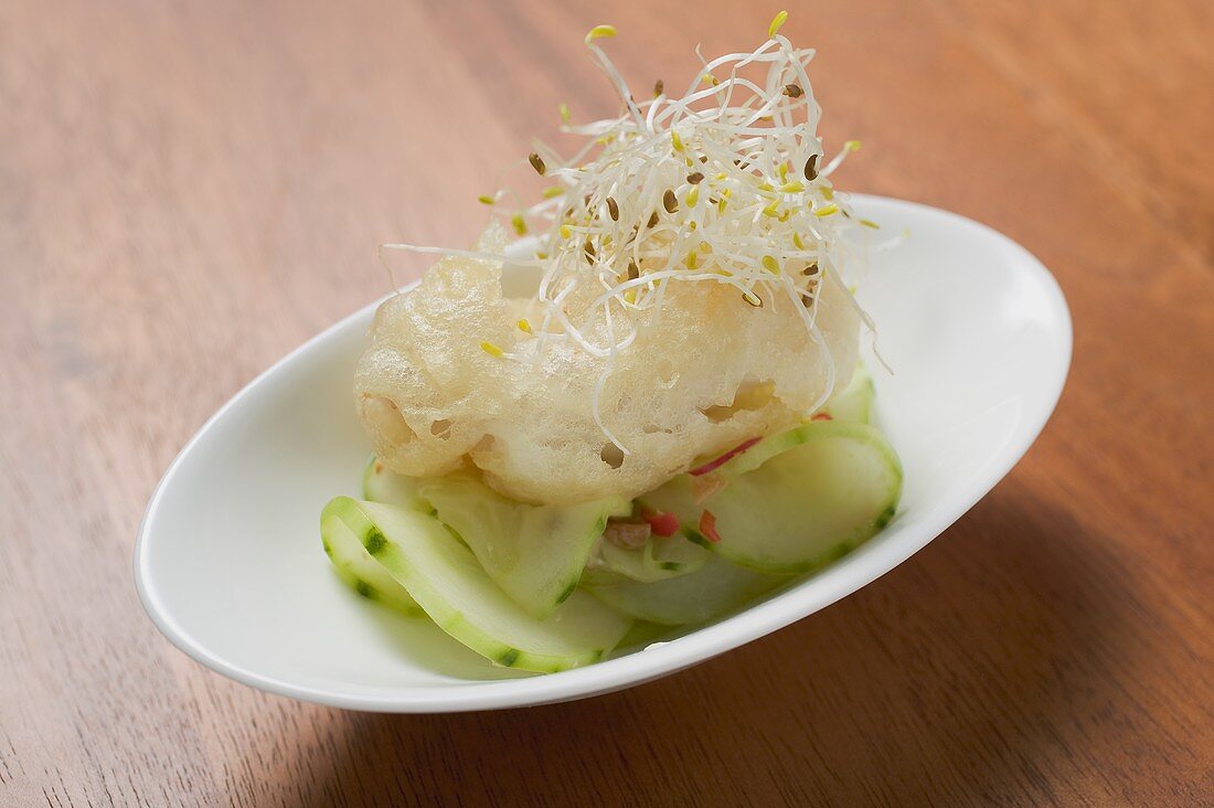 Ein Tempura-Häppchen auf scharfem Gurkensalat mit Keimlingen