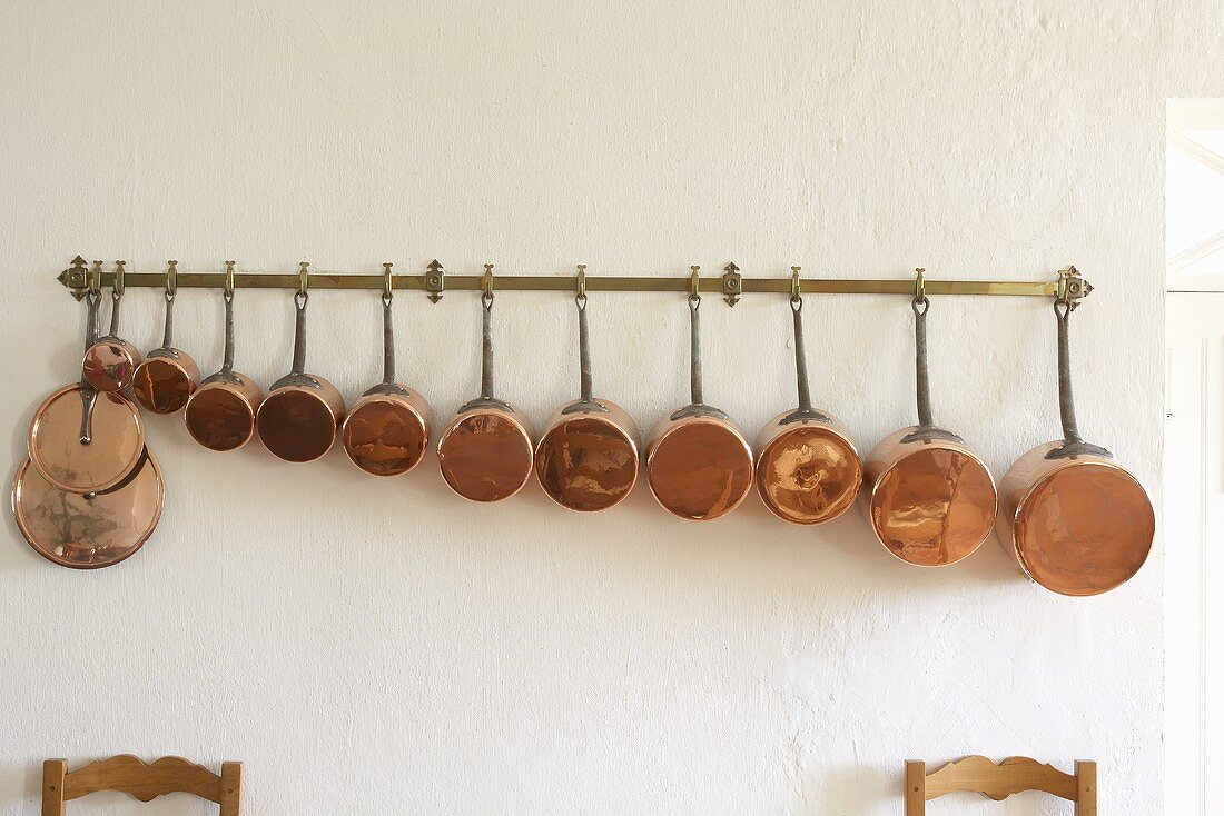 Copper pans of various sizes hanging on a rail