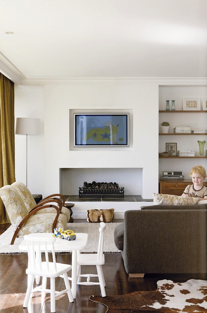 Wohnzimmer mit Fernsehgerät über dem offenen Kamin und Wandnische als Regalwand; im Vordergrund ein spielendes Kind