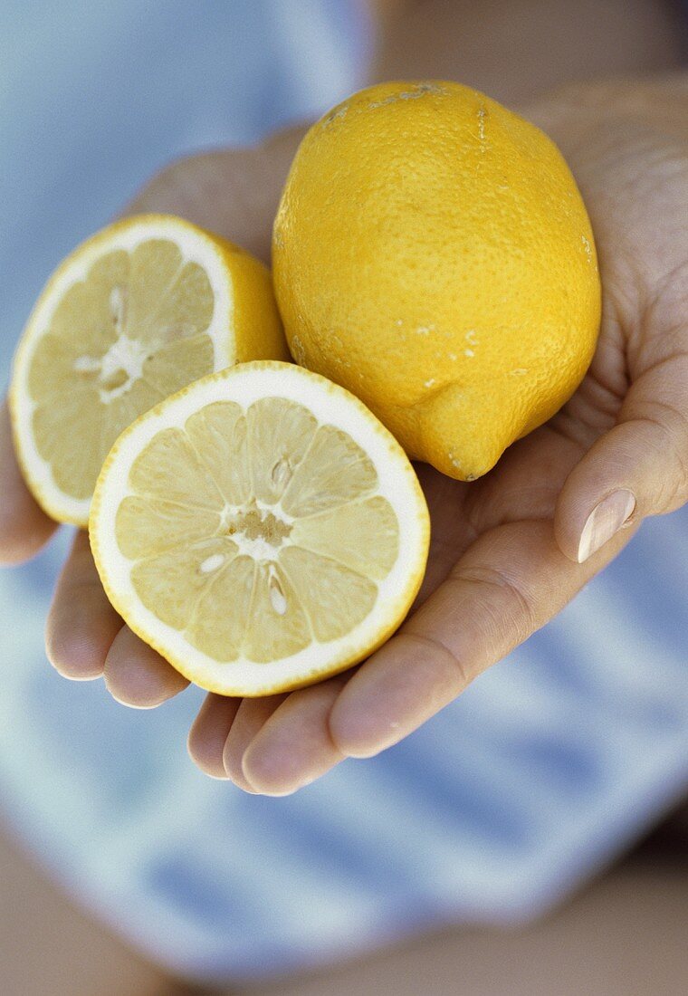 Hands holding one whole and one halved lemon