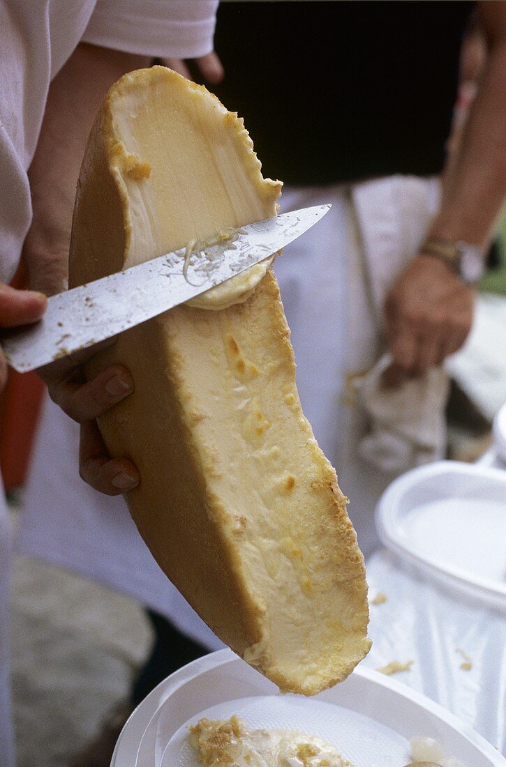 Geschmolzener Raclettekäse wird mit Messerrücken abgeschabt