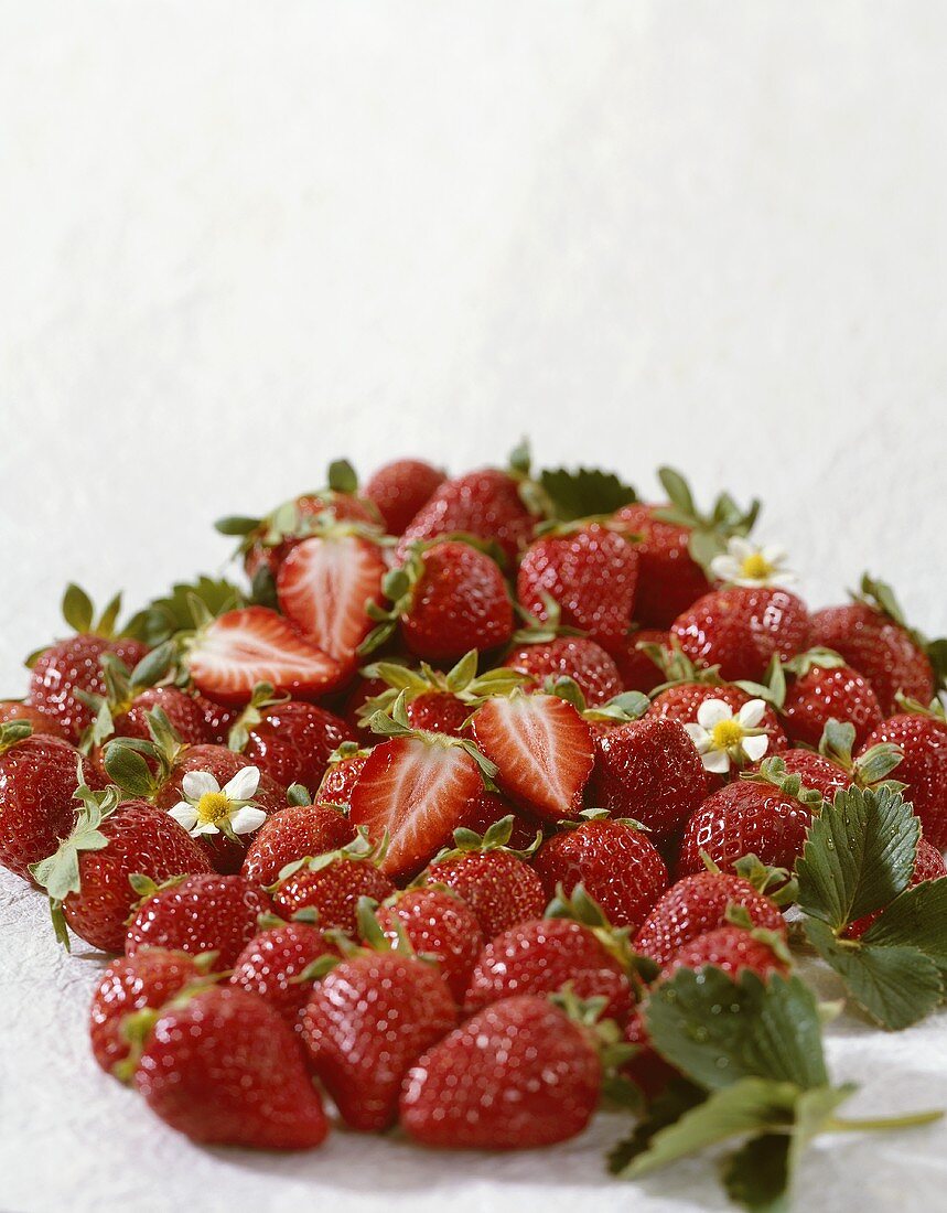 Ganze und halbierte Erdbeeren mit Blättern und Blüten