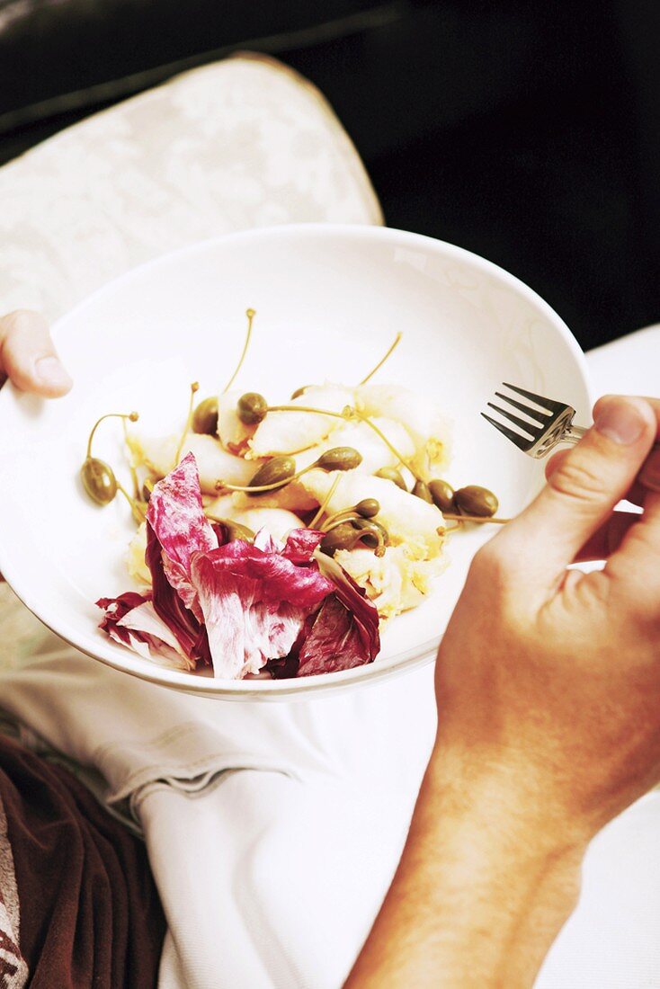 Man eating salad with capers and radicchio