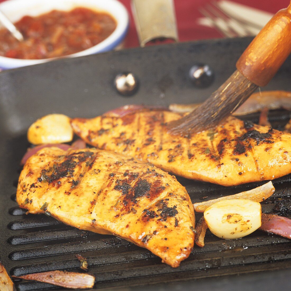 Brushing chicken breasts in a grill frying pan with marinade