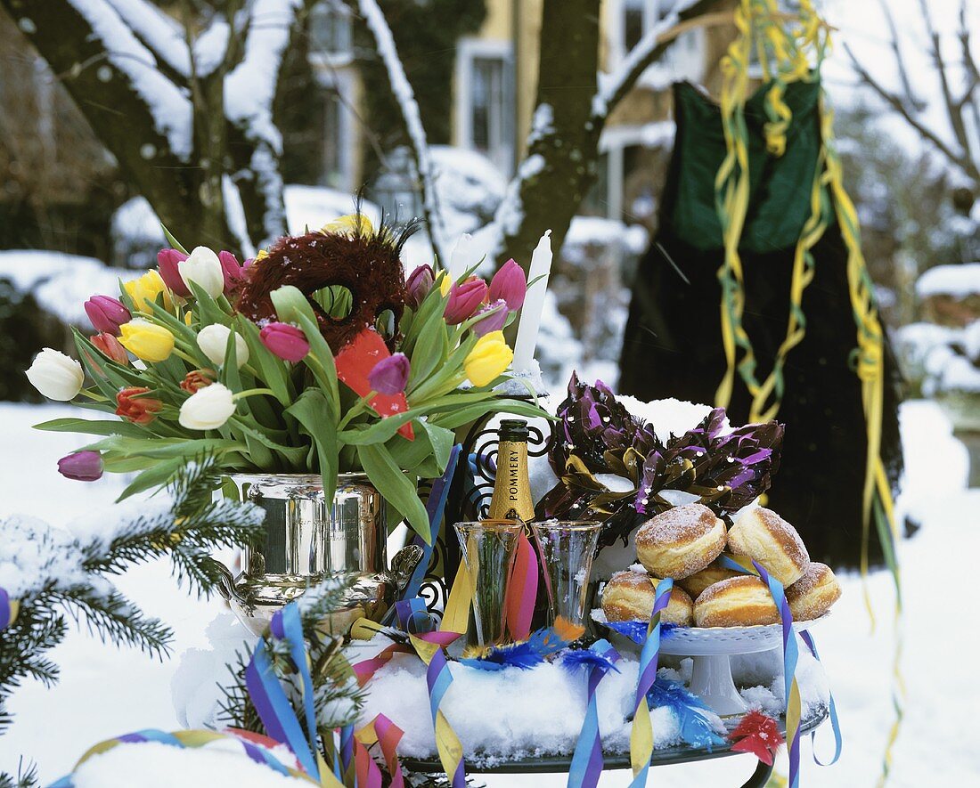 Krapfen, Champagner und Tulpenstrauss auf verschneitem Tisch