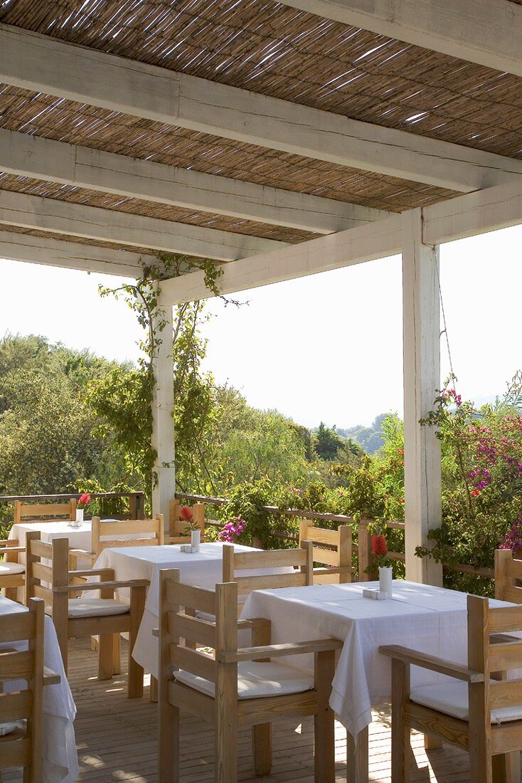 Holztische & Holzstühle auf überdachter Terrasse eines Restaurants