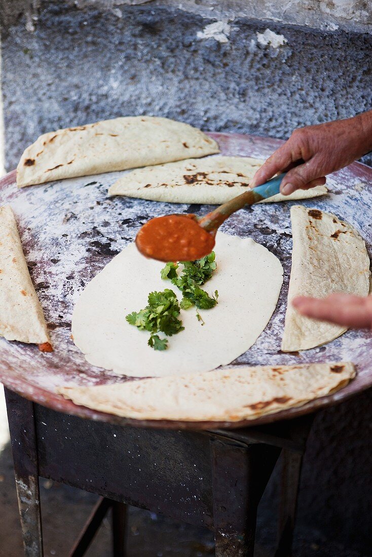A tortilla being spread with bean sauce