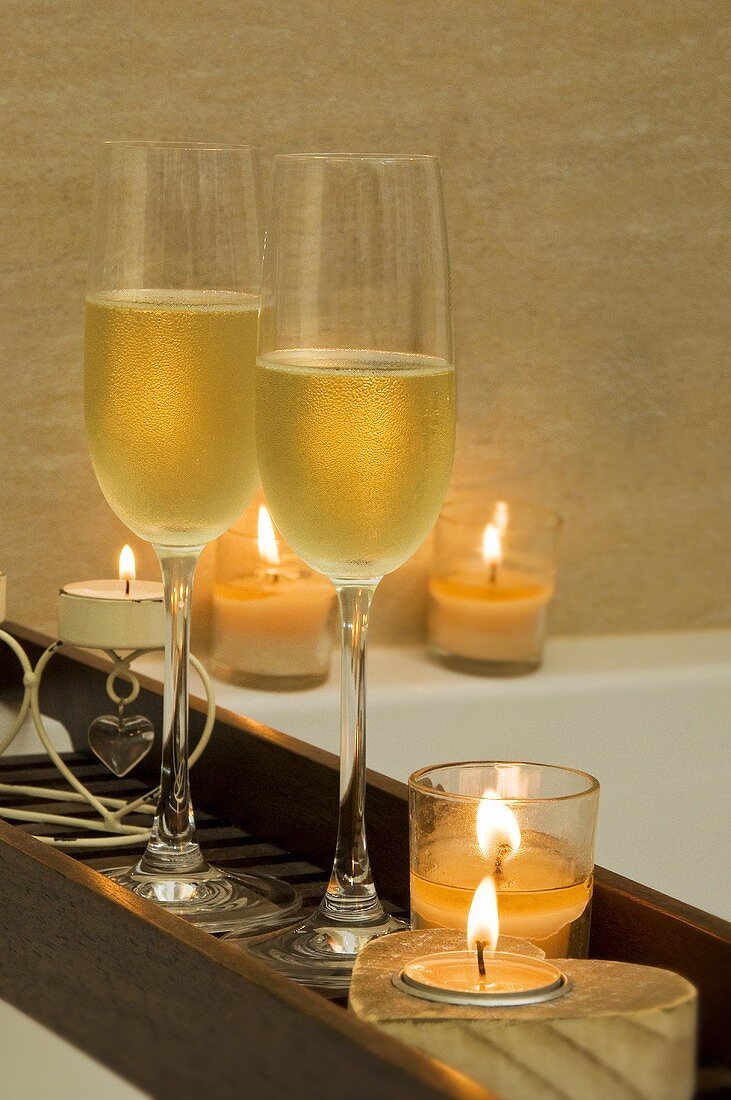 Two glasses of champagne and candles on a tray over a bath tub