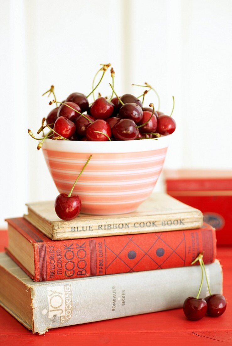 A bowl of cherries on a stack of old cook books