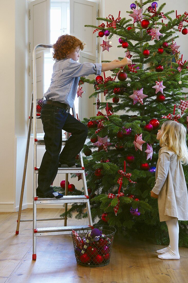 Zwei Kinder schmücken den Weihnachtsbaum