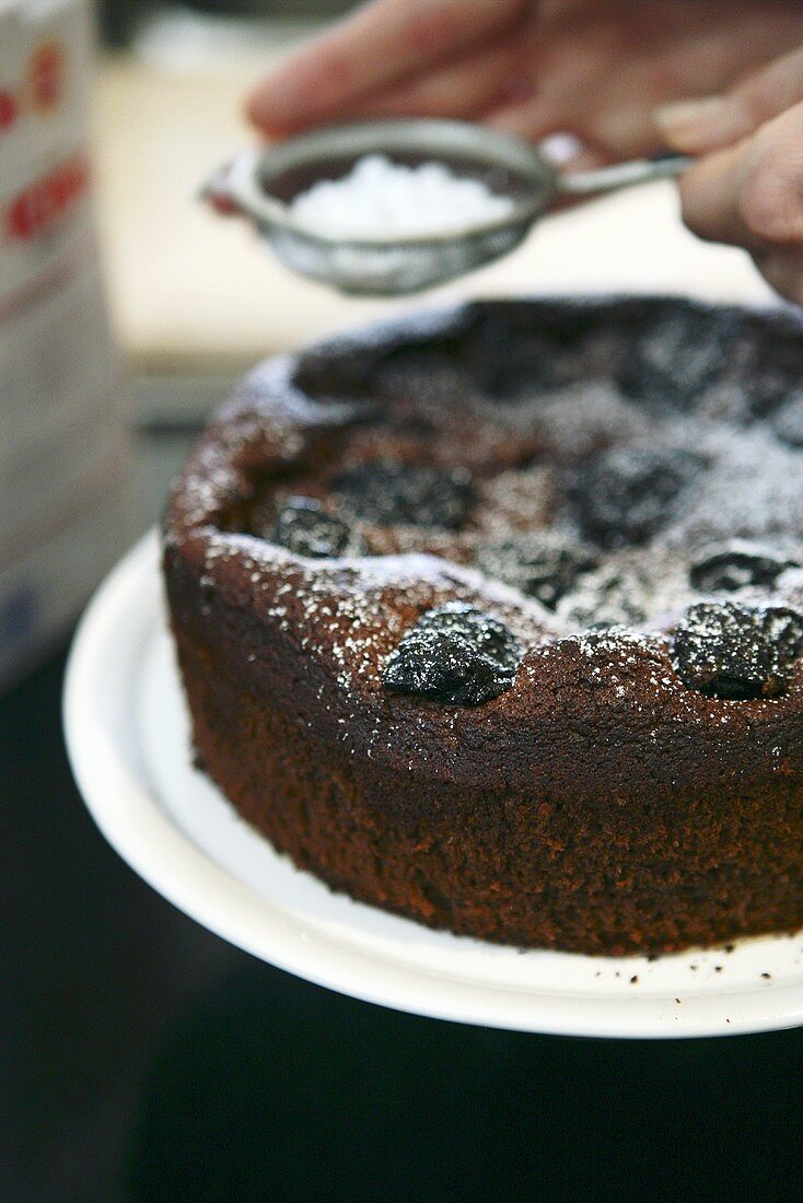 Schoko-Trockenpflaumen-Kuchen mit Puderzucker bestreuen