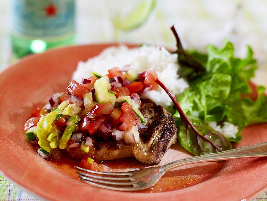 A pork chop with tomato salsa, rice and a green salad