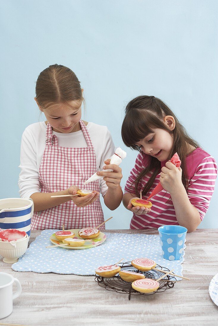Zwei Mädchen verzieren gebackene Lollis mit Zuckerglasur