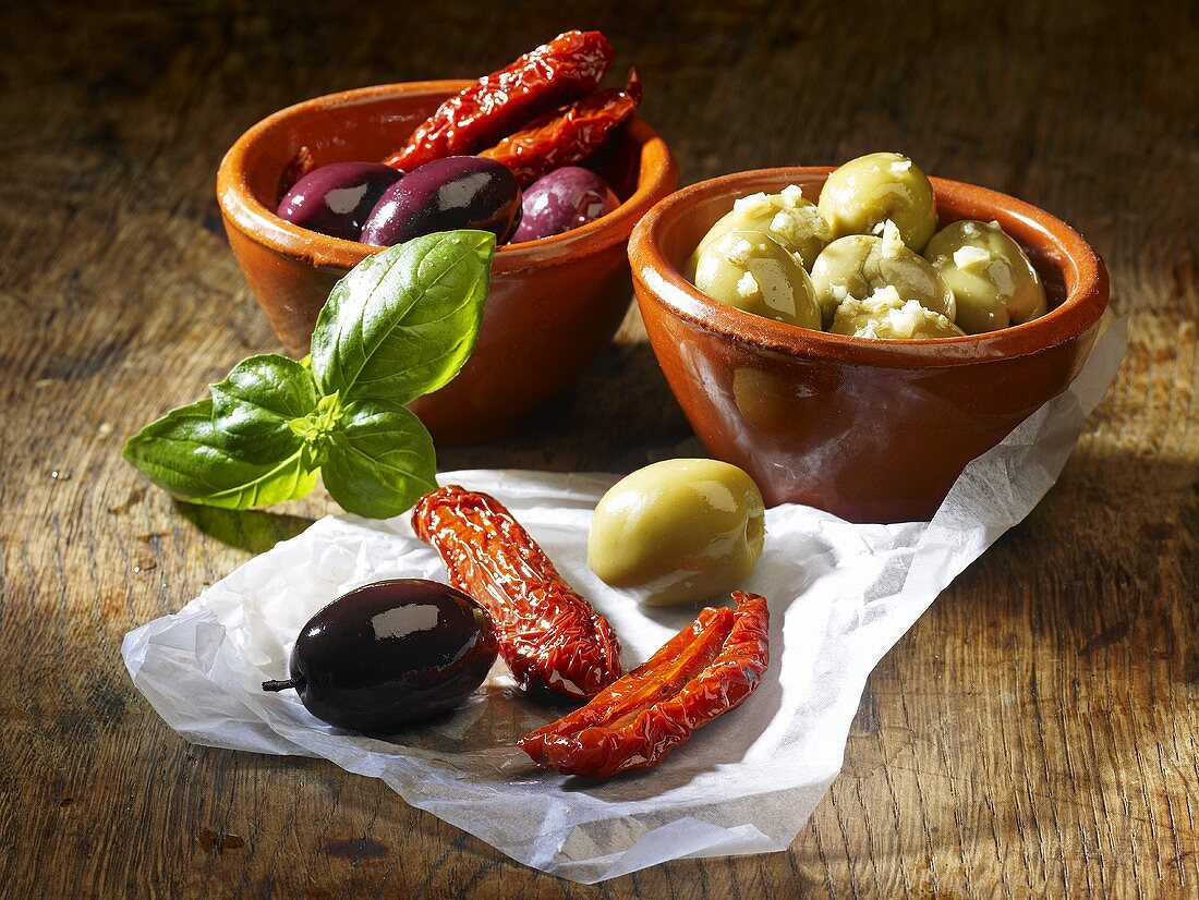 Dried tomatoes, olives and basil on a wooden surface