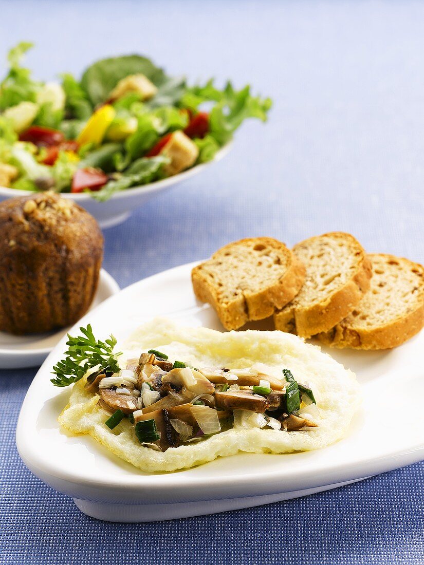 Eiweiss-Omelett mit Pilzen, Brot, im Hintergrund Muffin und Salat