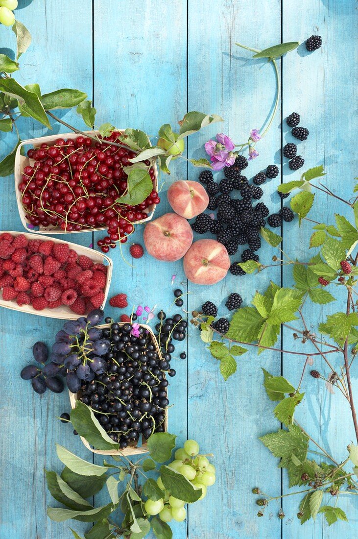 Berries, peaches, grapes and leaves on wooden background