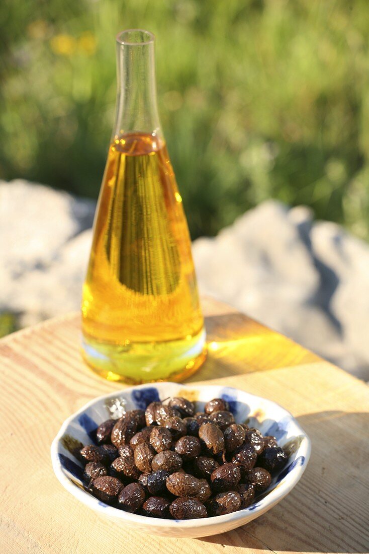 Olivenöl in Karaffe und Schale mit Oliven im Freien
