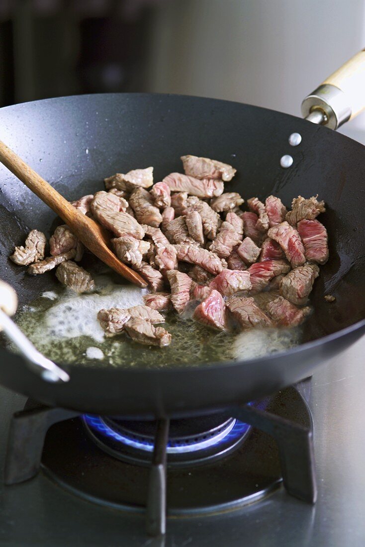 Sweating small pieces of beef in a wok over a gas flame