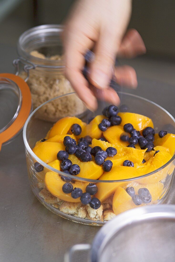 Hand streut Blaubeeren in eine Schüssel für Pfirsich-Gratin