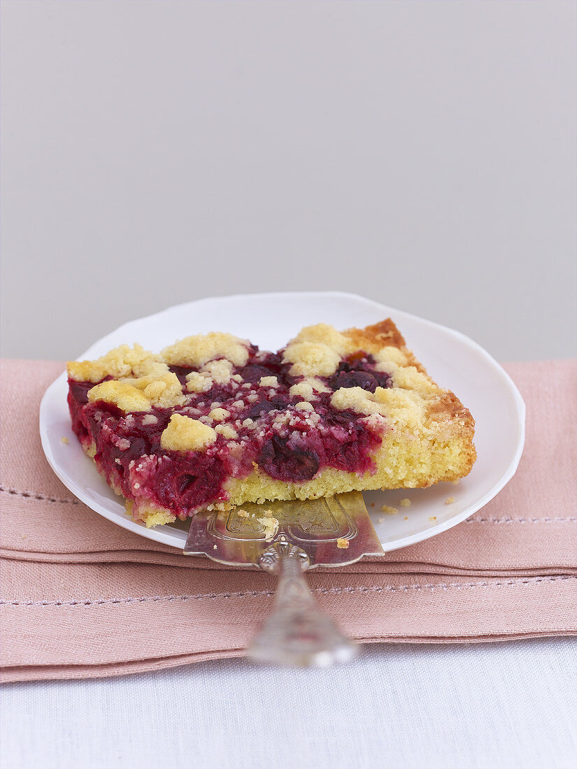 A piece of cherry crumble cake with cake slice