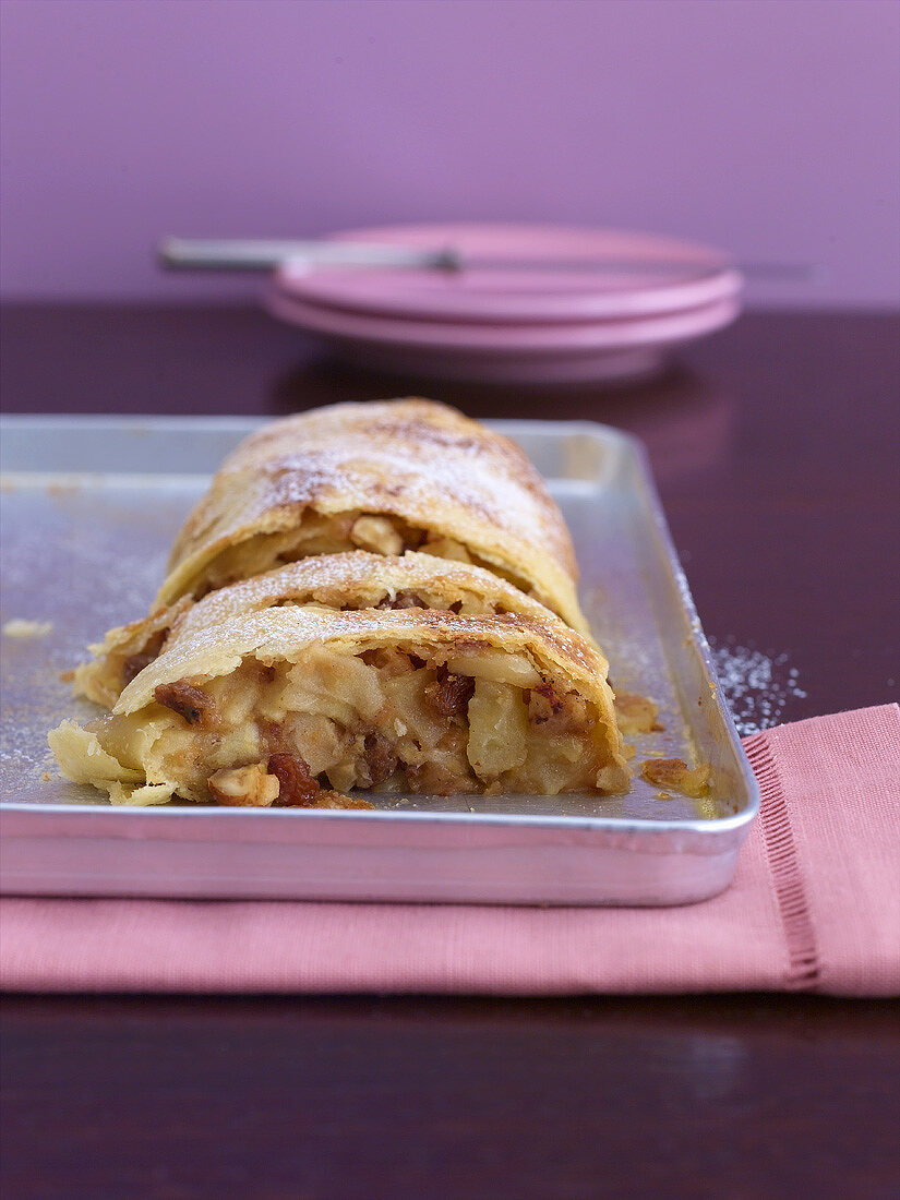 Partly sliced apple strudel on a baking tray