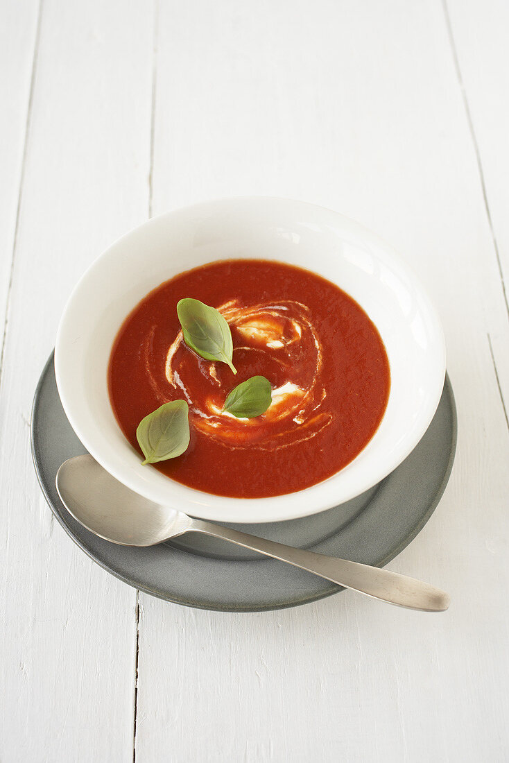A plate of tomato soup with basil leaves