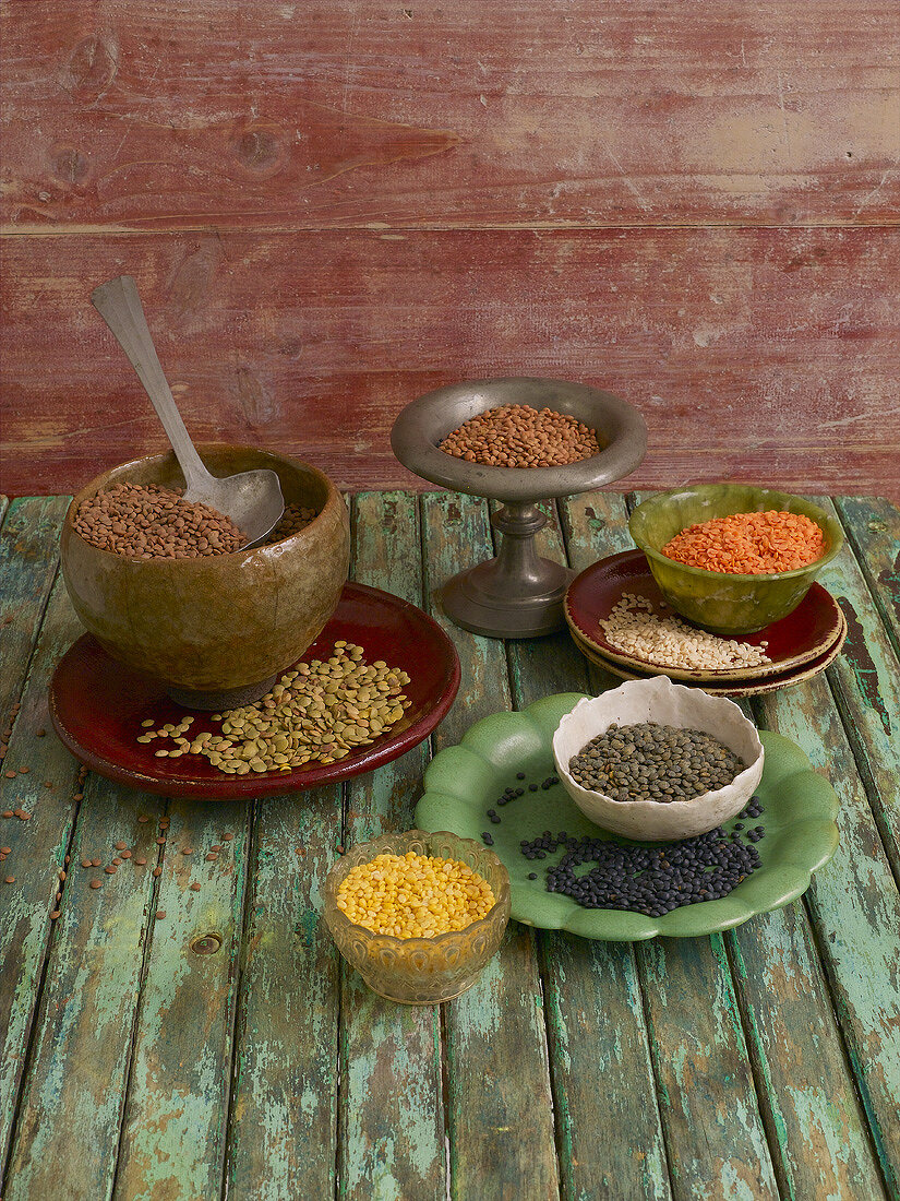 Various types of lentils in bowls on wooden background