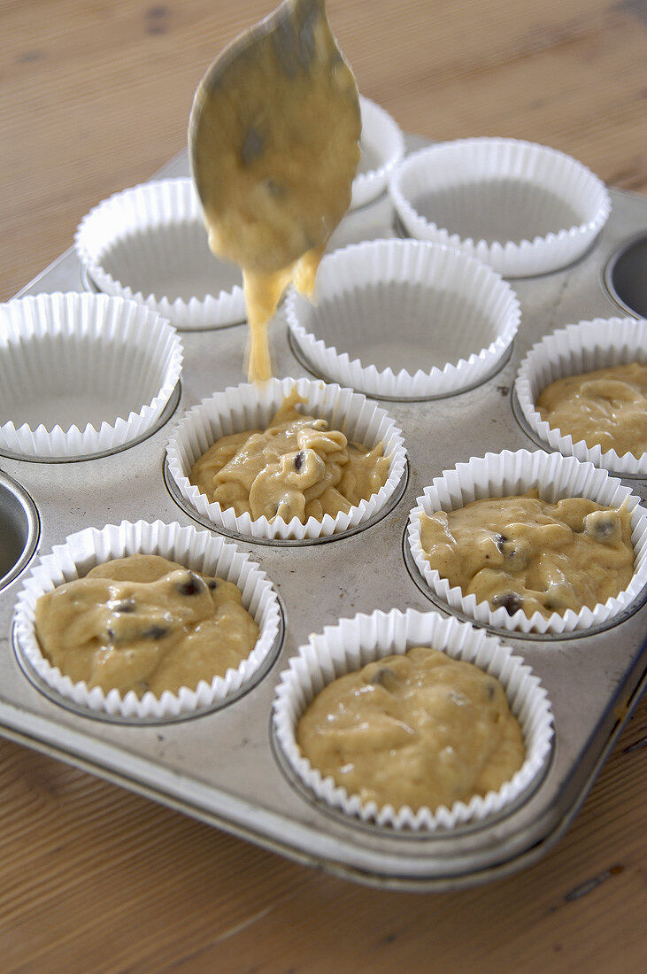 Filling muffin tin with banana & chocolate muffin mixture