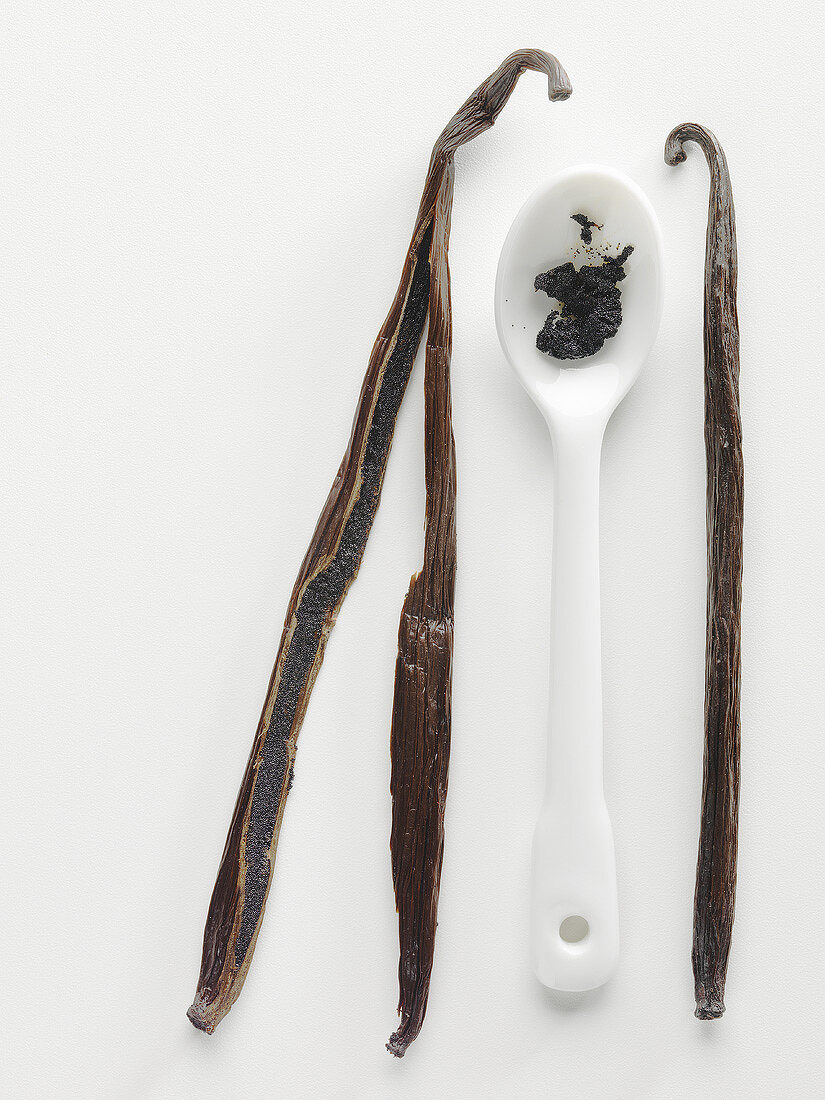 Three whole vanilla pods and vanilla seeds on a spoon