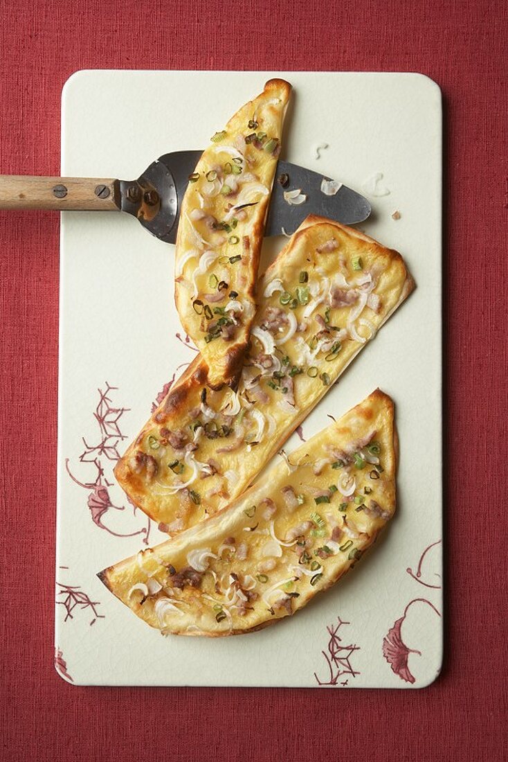 Three pieces of tarte flambée on a chopping board