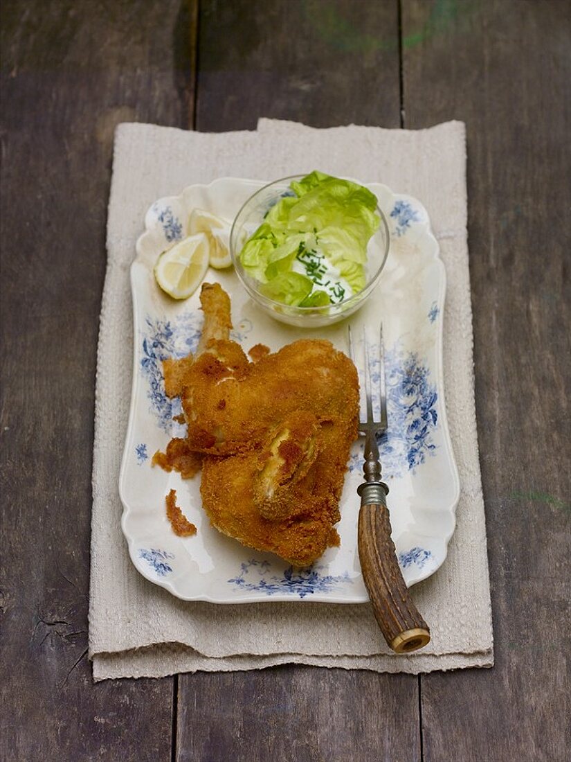 Half a fried chicken with lettuce on wooden background