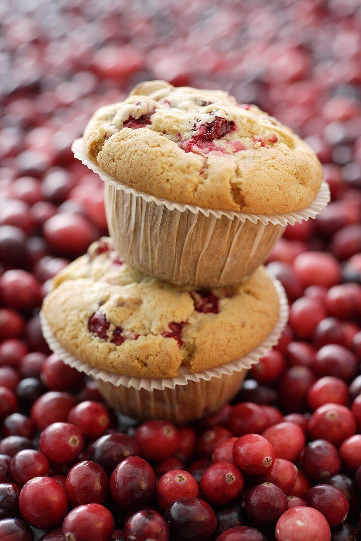 Two cranberry muffins, one on top of the other on cranberries