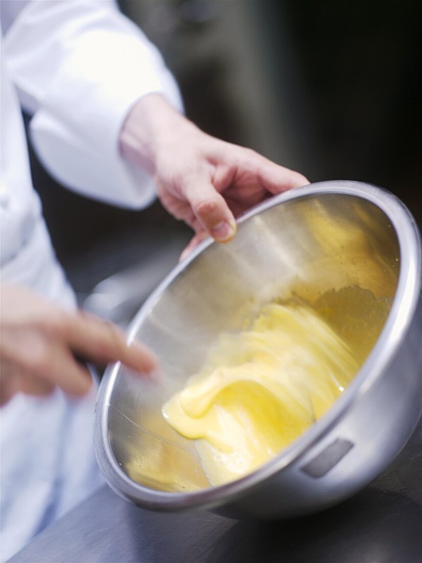 Chef beating a sauce in a mixing bowl