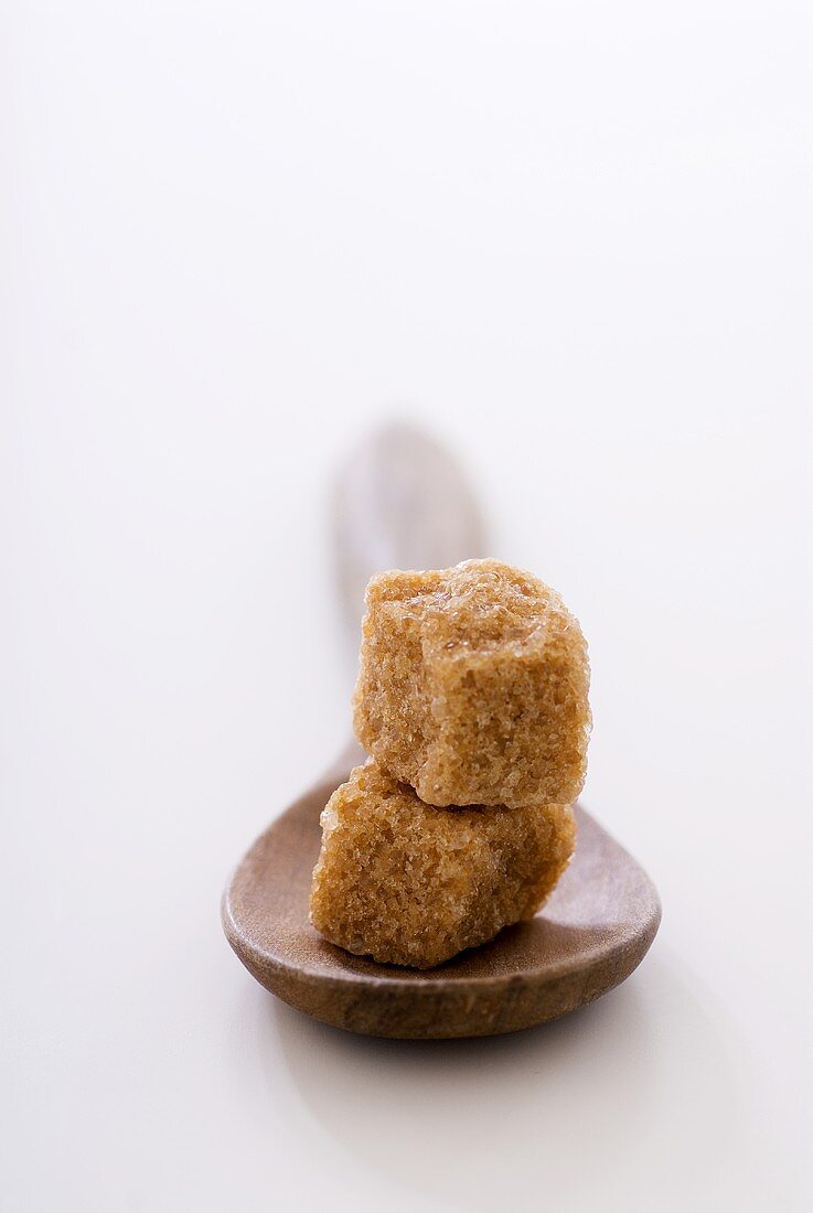Two brown sugar cubes, one on top of the other, on wooden spoon