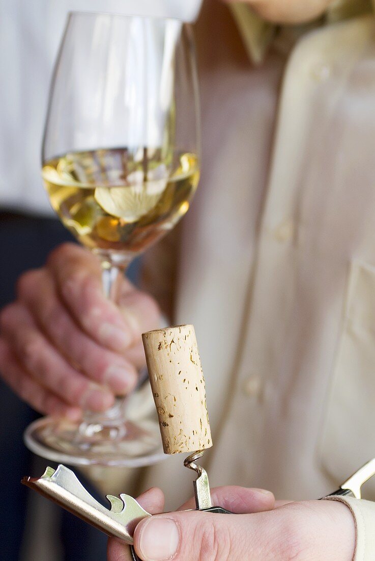 Mann hält Weinkorken mit Korkenziehen und Weissweinglas
