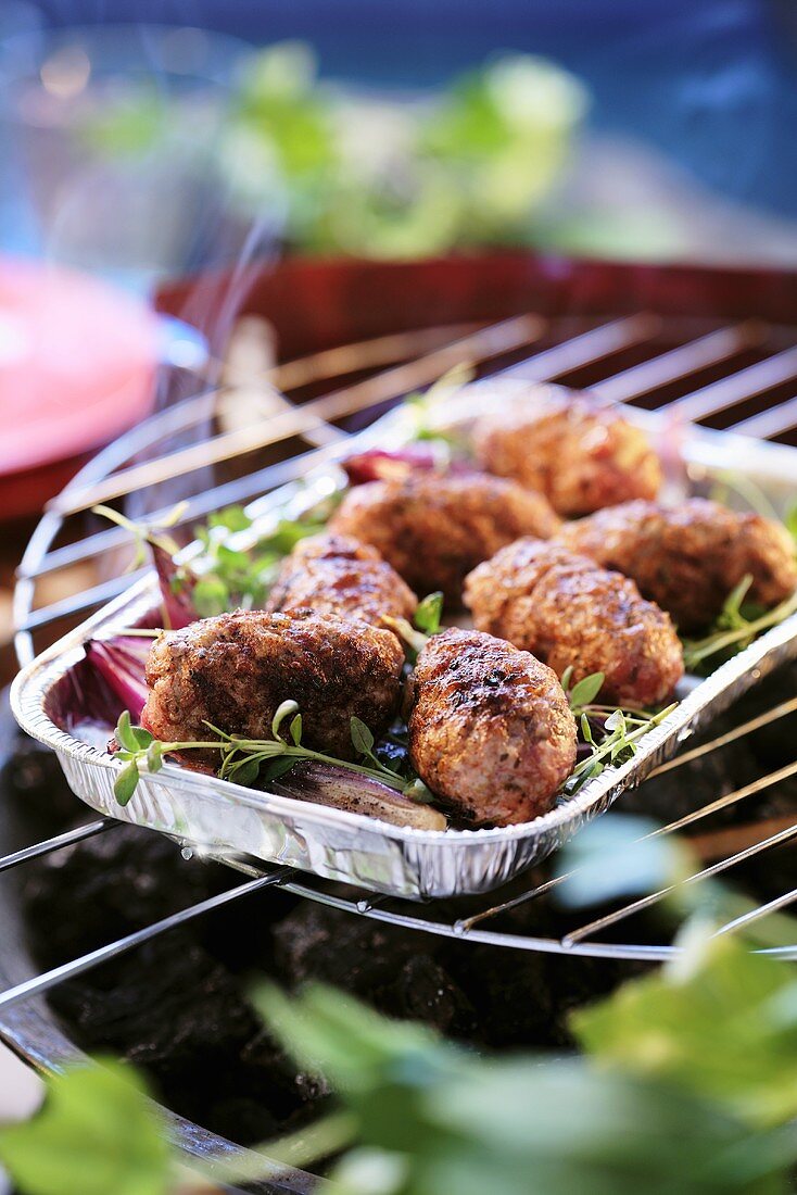 Cevapcici with herbs in an aluminium dish on a barbecue