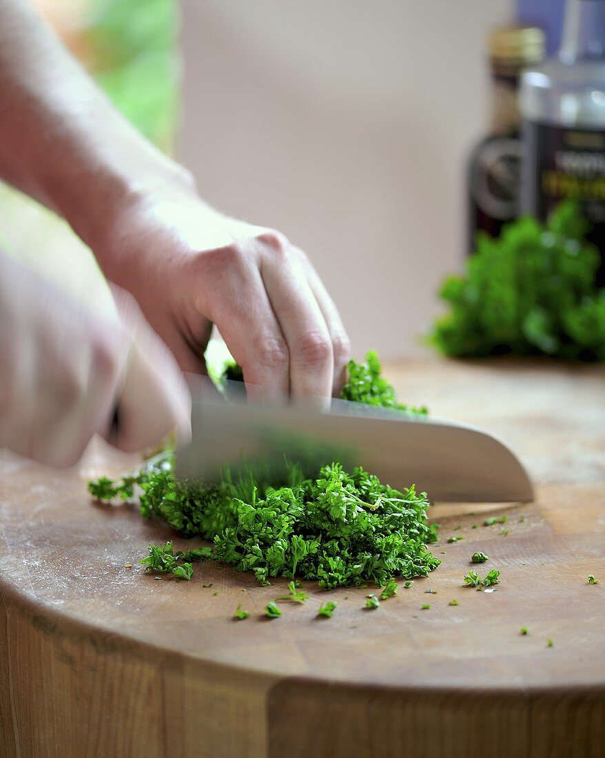 Man chopping curly parsley on wooden surface
