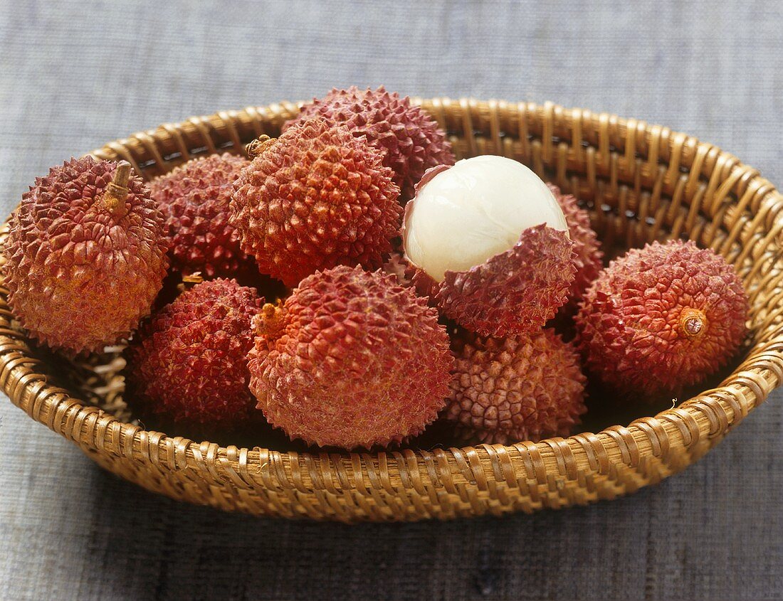 Lychees, one half-peeled, in a small basket