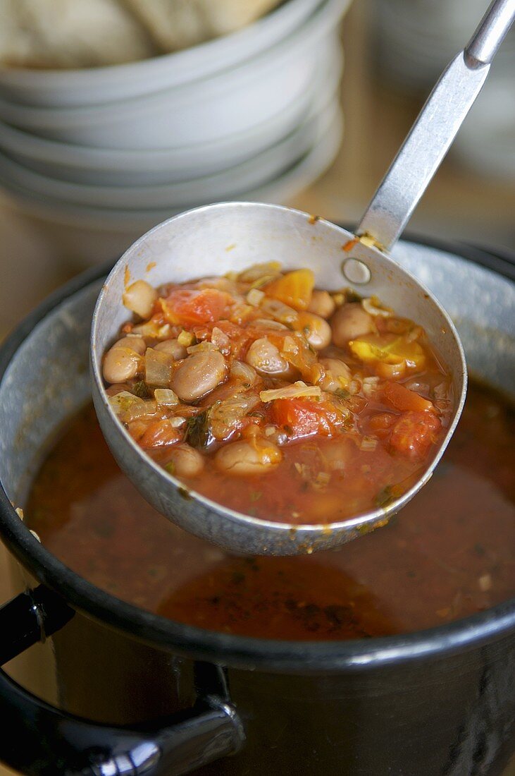 Tomaten-Flageoletbohnensuppe in einem Topf und Schöpfkelle