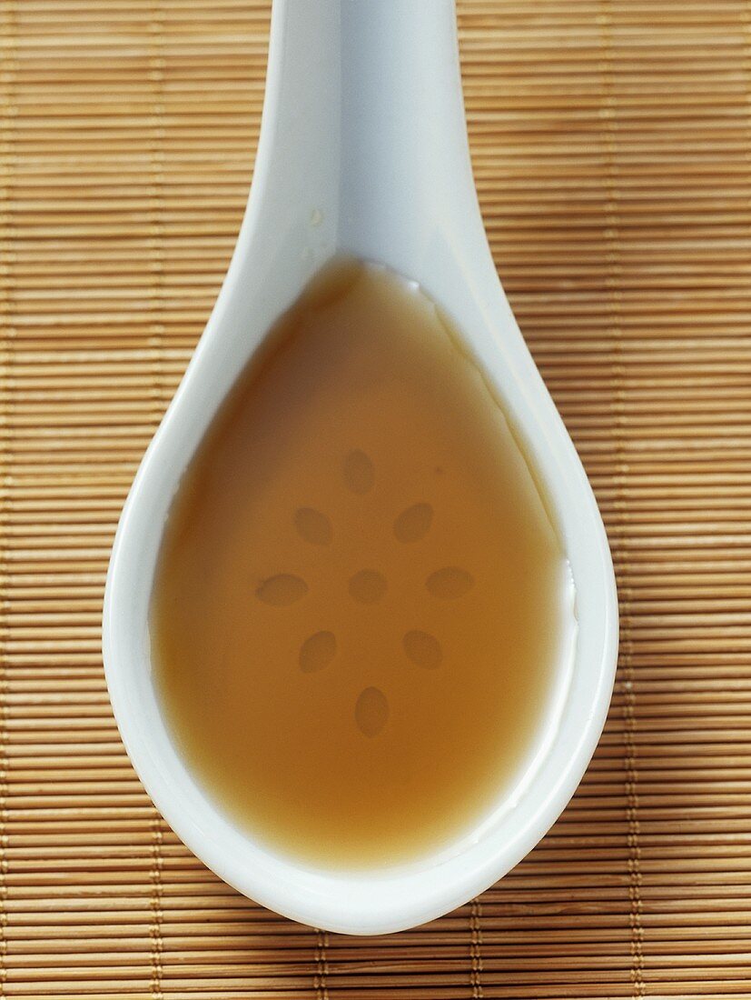 Sesame oil in a china spoon on a bamboo mat
