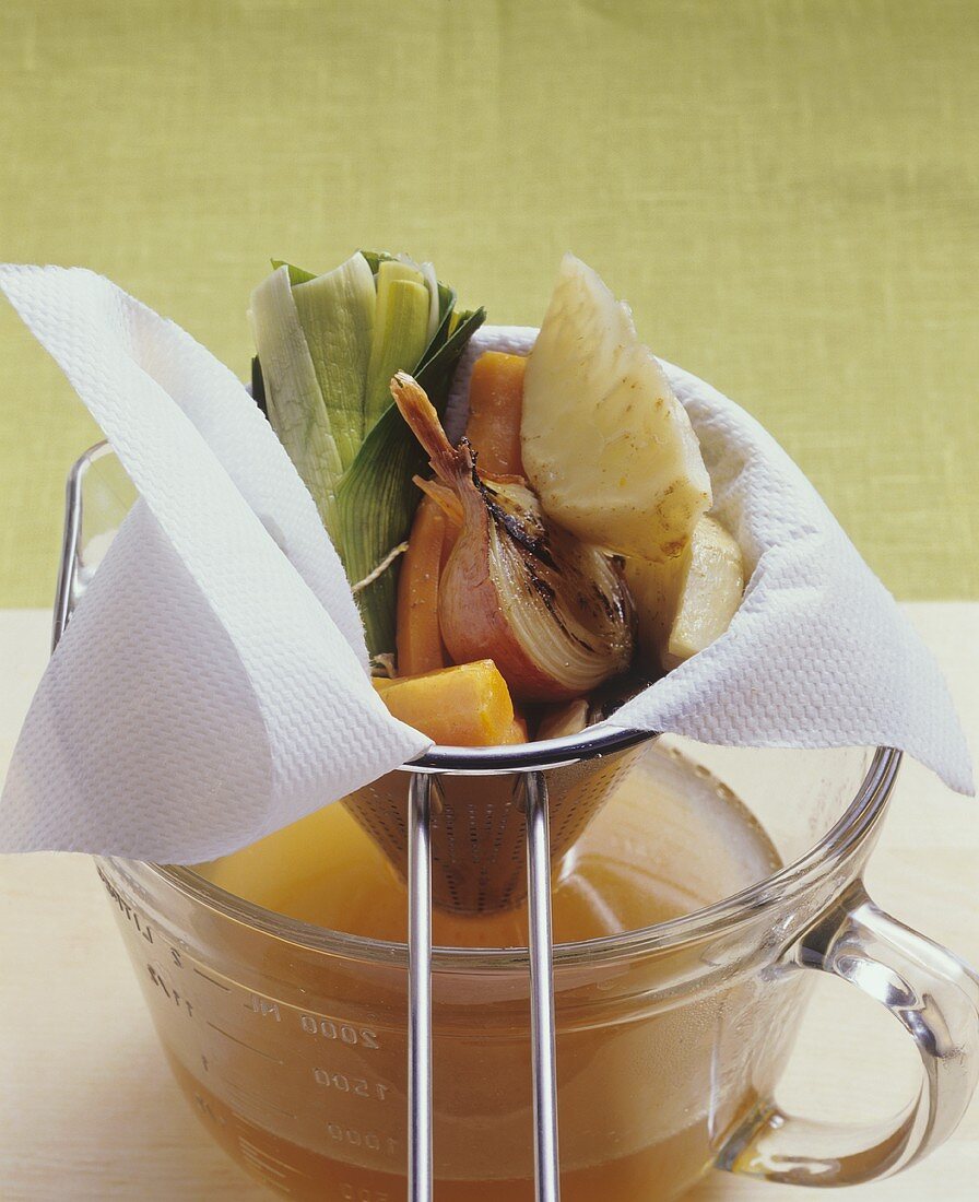 Straining beef stock through a sieve lined with a cloth