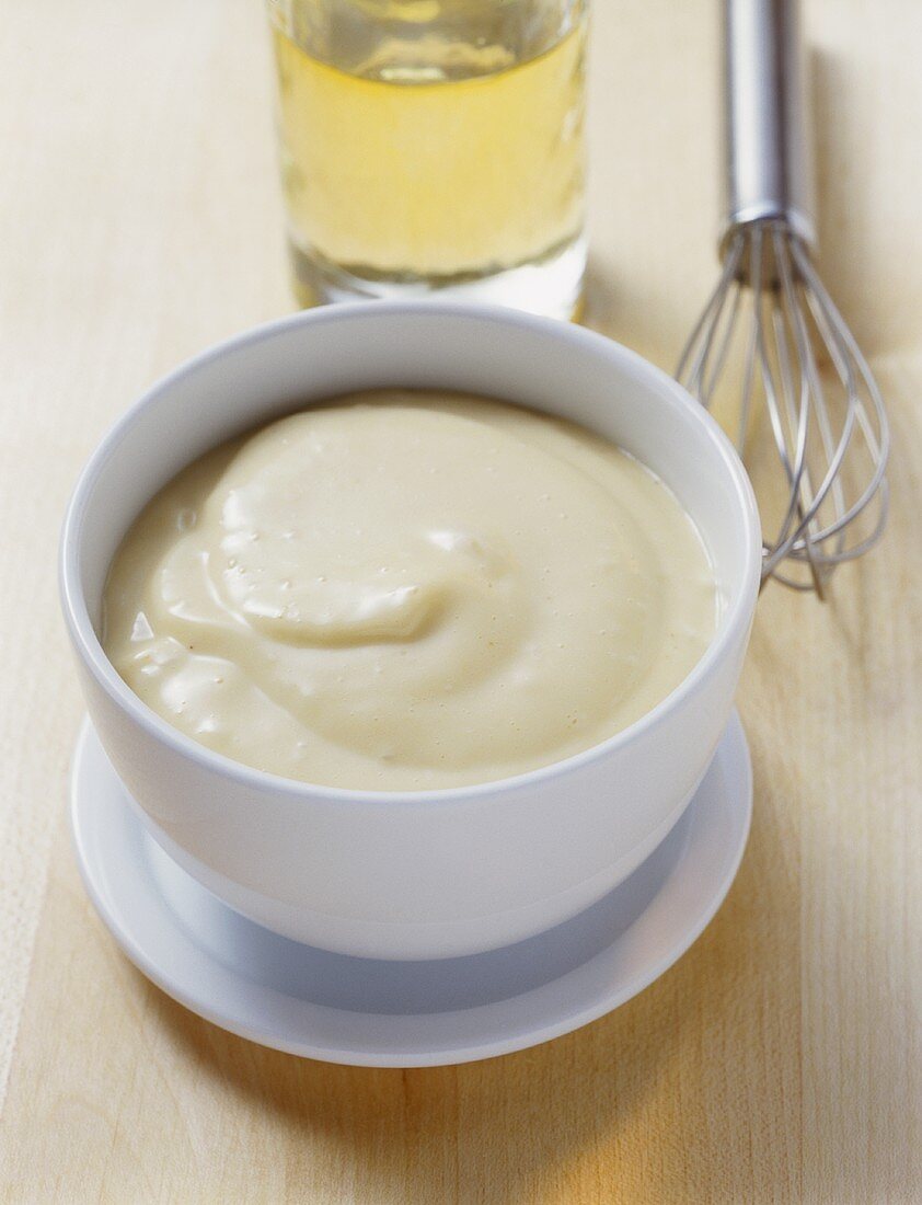 Mayonnaise in a bowl with bottle of oil and whisk