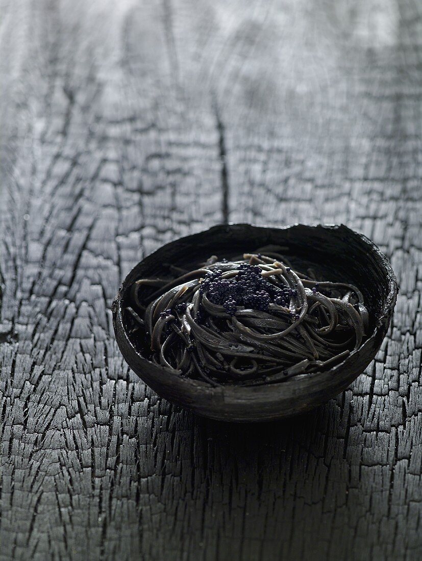 Schwarze Tagliatelle mit Kaviar in einem Holzschälchen