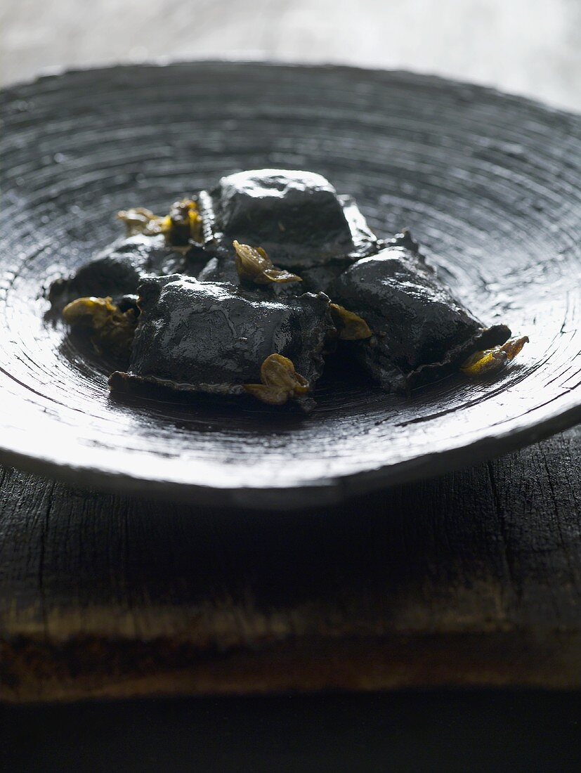 Black ravioli with capers on a wooden plate