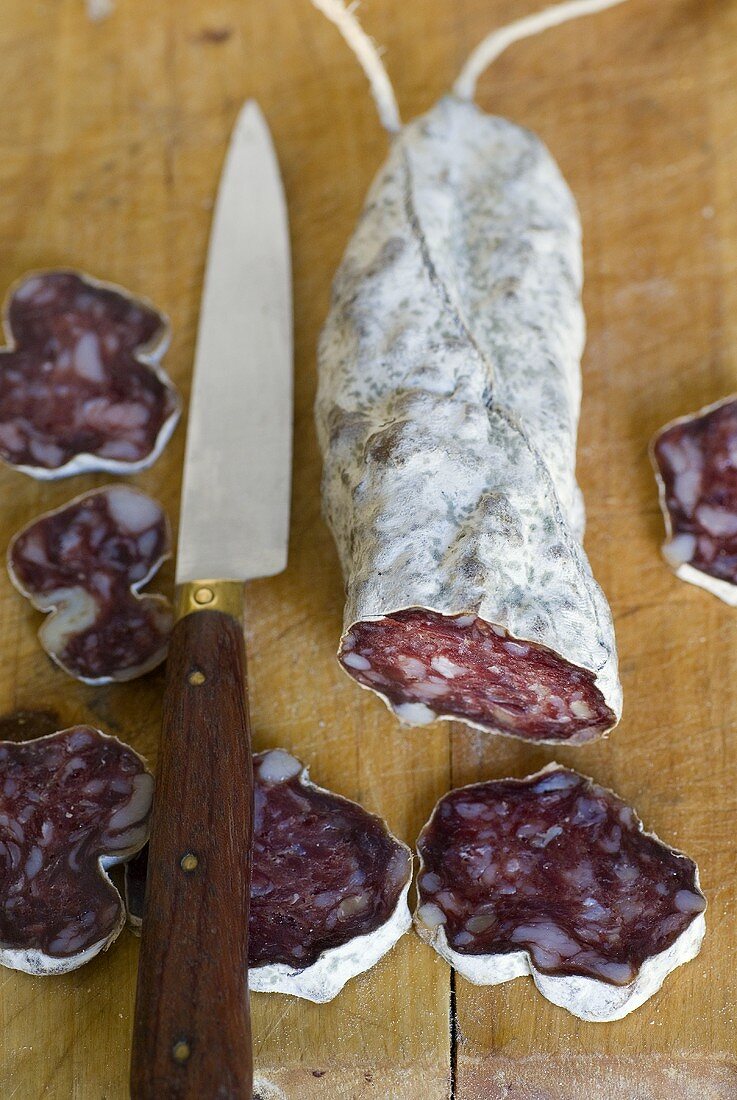 Partly-sliced salami on a wooden board with a knife